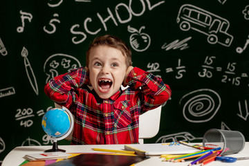 Emotional school boy sitting on the desk with many school supplies. First day of school. Kid boy from primary school. Back to school. Child from elementary school.