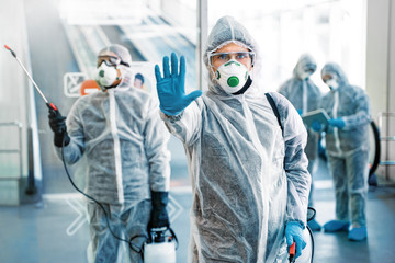 Fototapeta na wymiar Healthcare worker showing stop gesture. Team of healthcare workers wearing hazmat suits working together in shopping centre, to control an outbreak of virus in the city