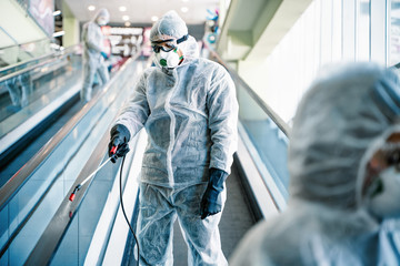 Disinfectant worker in protective suit making disinfection in shopping centre, to control an...