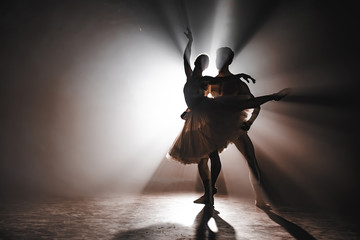 Graceful ballerina and her male partner dancing elements of classical or modern ballet in dark with floodlight backlight. Couple in smoke on black background. Art concept. - obrazy, fototapety, plakaty