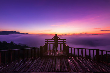 Tourist stand on wooden terrace during a beautiful early morning sky with twilight and waves of fog at Baan Ja Bo village viewpoint of Pang Mapha, Mae Hong Son, Northern Thailand.