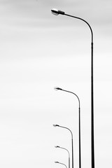 Black and white photo with the image of lampposts arranged in an even row against a cloudy sky.