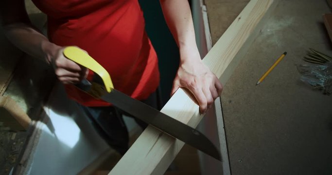 Pregnant woman sawing a wooden post in the loft