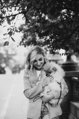 Beautiful young blond woman with her pet Pomeranian dog breed for a walk. Little fluffy dog. Black and white art photo. Soft selective focus.