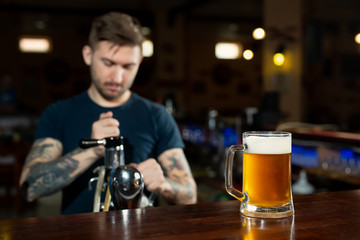 Bartender pouring from tap fresh beer into the glass in pub