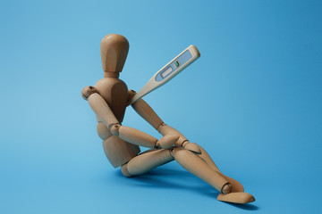 Wooden man figure is sitting with a degree meter/thermometer . Concept of fatigue from a long illness and high fever. 39 degrees Celsius on a clinical electronic thermometer.