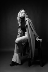 Beautiful girl wearing a casual trendy trousers, turtleneck and raincoat posing on a dark background. Fashionable, advertising, lifestyle and commercial monochrome design.