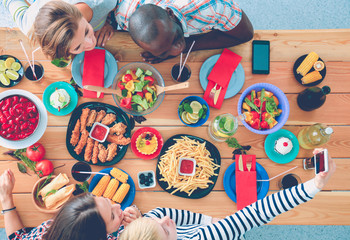 Top view of group of people having dinner together while sitting at wooden table. Food on the table. People eat fast food.