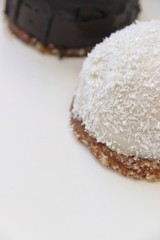 Extreme closeup of two raw cakes, the one with coconut and one with chocolate on white plate. Macro, vertical, shallow DOF.