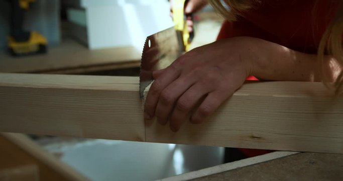 Young pregnant woman sawing wooden post an dblowing sawdust away