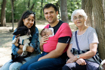 Fototapeta premium Happy Family with Baby in Sling and Dog in the Park .Family Portrait with Dog