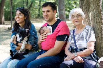 Fototapeta premium Happy Family with Baby in Sling and Dog in the Park .Family Portrait with Dog