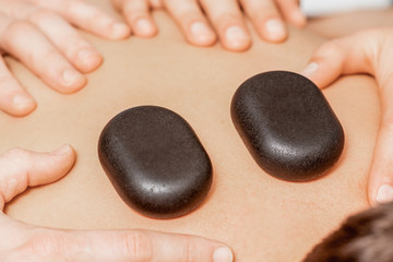 Fototapeta na wymiar Hands of massage therapists doing back massage while hot stones on back of man close up in spa.