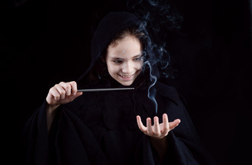 A girl in a witch's cloak with a magic wand in his hand conjures magic. Halloween outfit