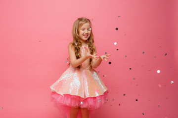 happy Little girl catches confetti on pink background, holiday concept