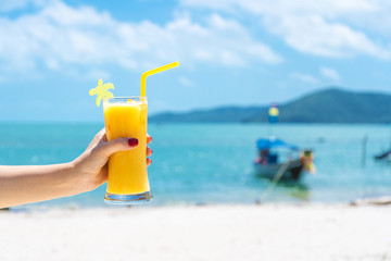 Fototapeta na wymiar First-person view. Girl holds a glass cup of cold mango fresh on the background of a sandy tropical beach. White sand and a boat. Fairytale vacation in Thailand