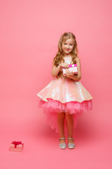 a little girl holding a gift in her hands smiles on a pink background.