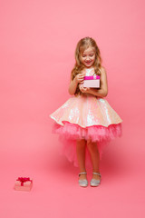 a little girl holding a gift in her hands smiles on a pink background.