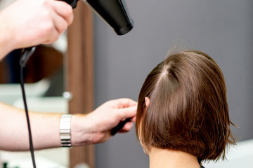 Fototapeta premium Close up of professional hairdresser is drying hair of woman, back view in hair salon.