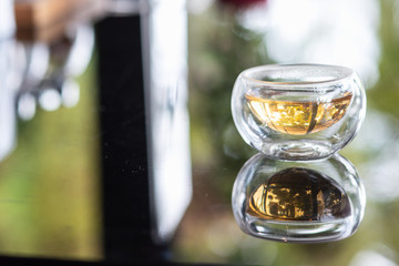 The syrup in clear cup on mirror surface with reflection.