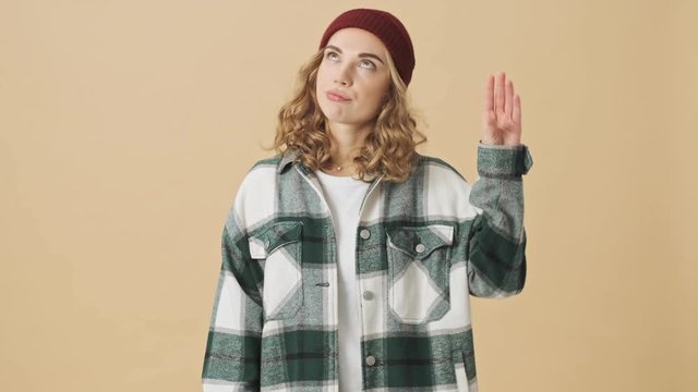 Bored pretty woman in knit hat and shirt showing blah blah blah gesture and looking away over beige background