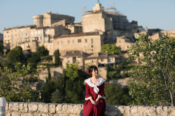 Fototapeta na wymiar Young Asian woman in red dress, sitting at the edge of cliff outside the ancient village of Gordes, Provence, France