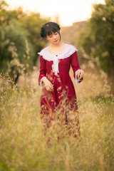 Young Chinese woman in red retro style dress, walking and traveling in a meadow field, France, Europe