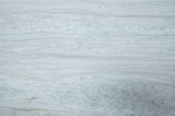 A polished slab of white marble with gray stripes and dots called Nestos Beige