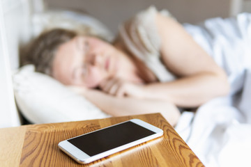 Young Eastern European woman sleeping in bed with mobile phone on the foreground