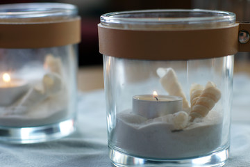 Two candles in transparent candlesticks with sand and a shell are on the table