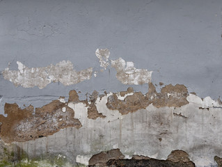 Gray plastered wall. Texture with falling plaster and traces of destruction