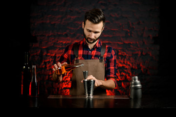 professional bartender pours liquor into metal jigger.