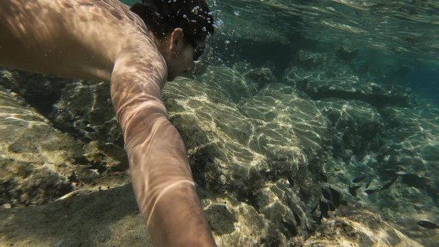 Self-recording video of a young man in his 20s snorkelling at the bottom of the Mediterranean Sea in Cyprus, filming sea life and looking at the camera.