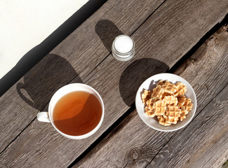 White cup of tea and waffles on rustic background with hard shadows of morning light. Minimal concept Hard deep shadow. Flat lay, top view