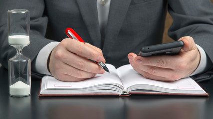business man in the office is working with a mobile phone on the background of an hourglass. business and successful goal