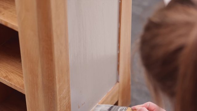 A young woman painting an oak cabinet in grey chalk paint close-up