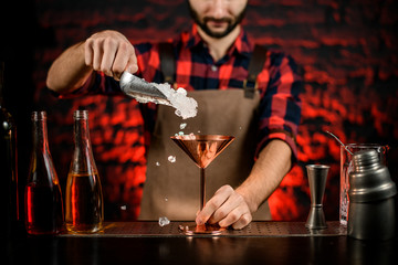 bartender hand pouring pieces of ice into metal martini glass.