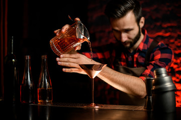 male bartender pours cocktail from bowl into metal martini glass.