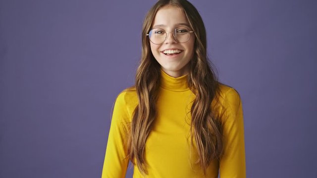 A positive young teenage girl is laughing isolated over a purple background in studio