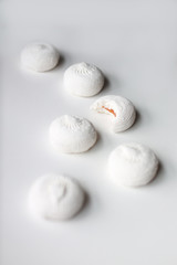 Six white sweet dessert zephyr marshmallows on white background with one bitten, close up perspective view