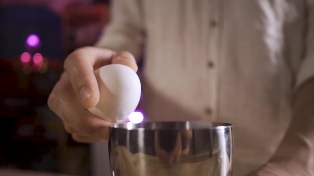 Close up Bartender's hands breaks the egg, protein flows out of the egg into the shaker . White shirt