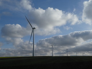 Obraz premium Row of five wind turbines surrounded by cottony clouds