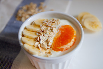 Healthy breakfast: yogurt with outmeal, banana and tangerine in a white bowl on the table