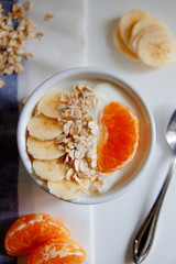 Healthy breakfast: yogurt with outmeal, banana and tangerine in a white bowl on the table
