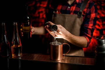 bartender neatly pours cocktail from jigger into metal cup.