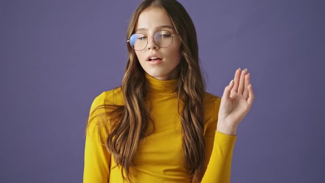 A displeased teenage girl is showing nonsense or boring content while gesturing her hand standing isolated over a purple background in studio