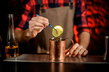 male bartender decorated metal cup by citrus slice.