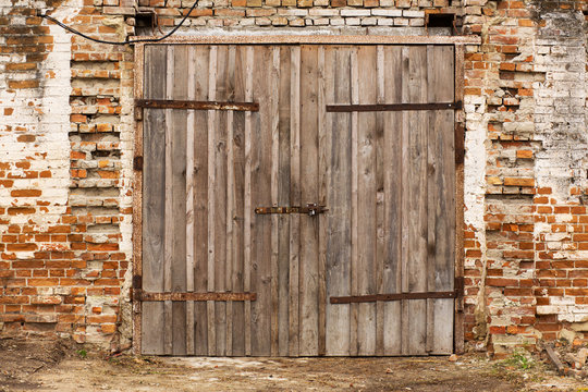 Old cowshed. Large wooden gate and dried wood. Old brick building