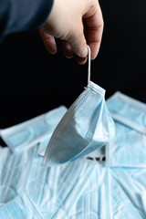 Protective masks on black background. Hand holding a used surgical mask with a background of unused surgical masks. Medical PPE