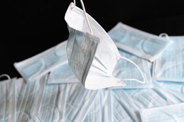 Protective masks on black background. Hand holding a used surgical mask with a background of unused surgical masks. Medical PPE